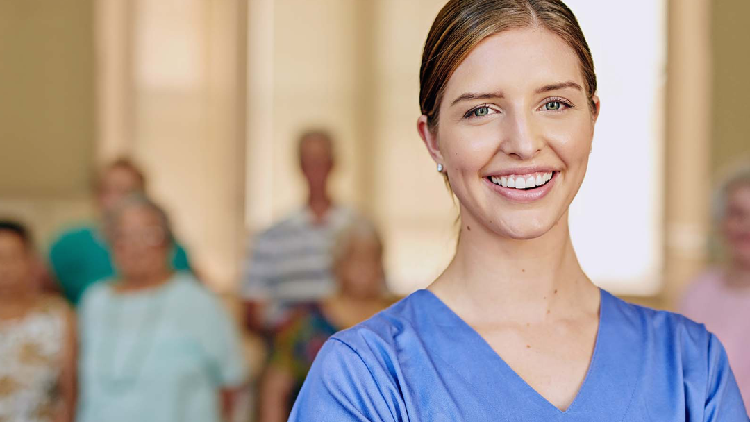 A smiling care worker with residents in the background.